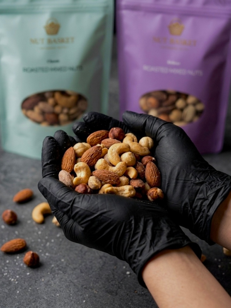 Hands holding a heap of mixed nuts with Nut Basket packaging in the background